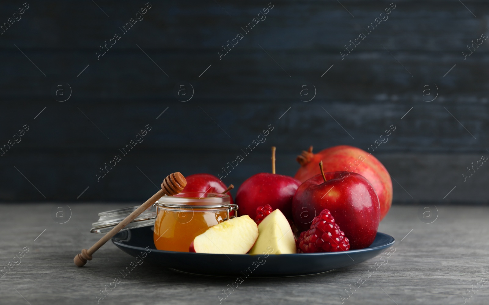 Photo of Honey, apples and pomegranate on grey table. Rosh Hashanah holiday