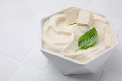 Photo of Delicious tofu sauce and basil leaf in bowl on white tiled table, closeup. Space for text