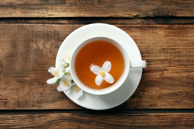 Cup of aromatic jasmine tea and fresh flowers on wooden table, top view
