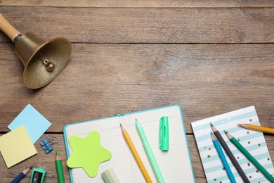 Different stationery and school bell on wooden background, flat lay. Space for text