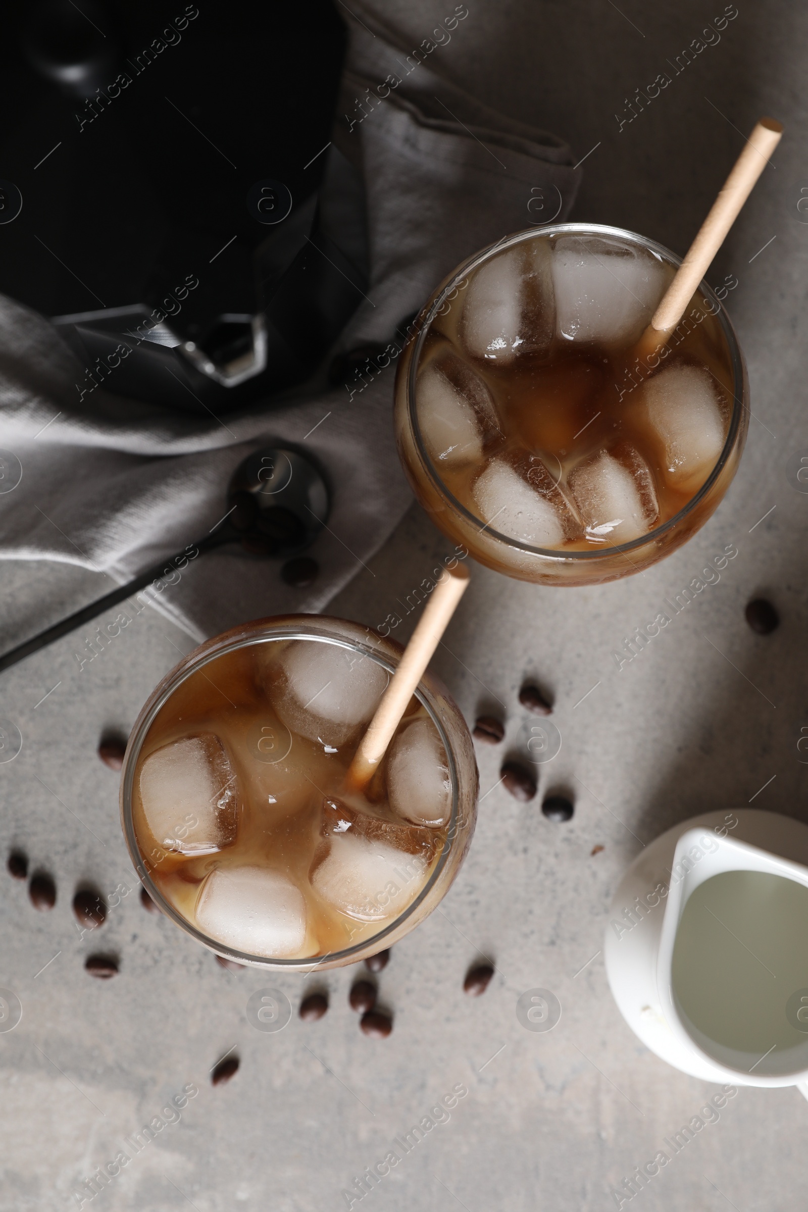 Photo of Refreshing iced coffee with milk in glasses, beans and spoon on gray table, flat lay