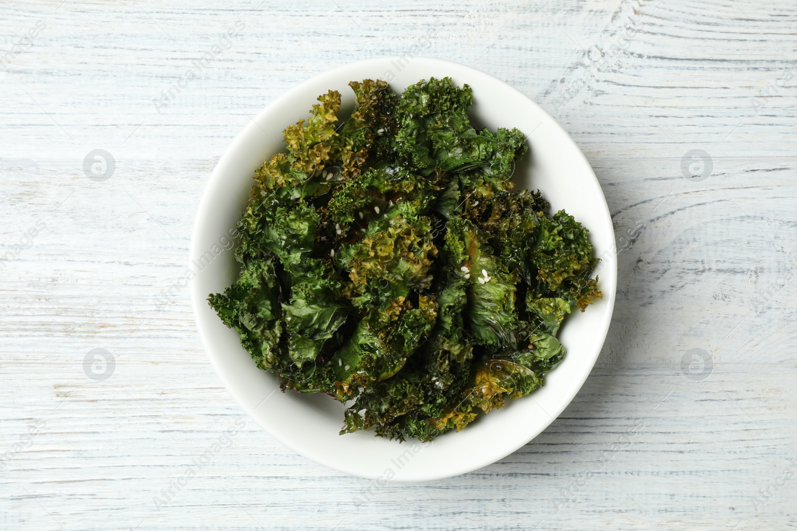 Photo of Tasty baked kale chips on white wooden table, top view