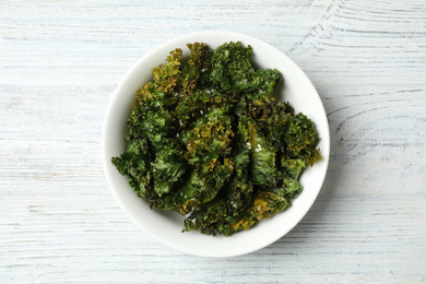 Photo of Tasty baked kale chips on white wooden table, top view