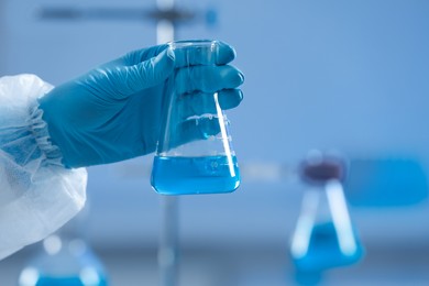 Photo of Scientist holding flask with light blue liquid in laboratory, closeup