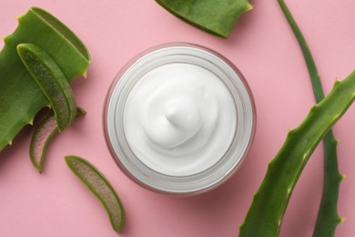 Jar with cream and cut aloe leaves on pink background, flat lay