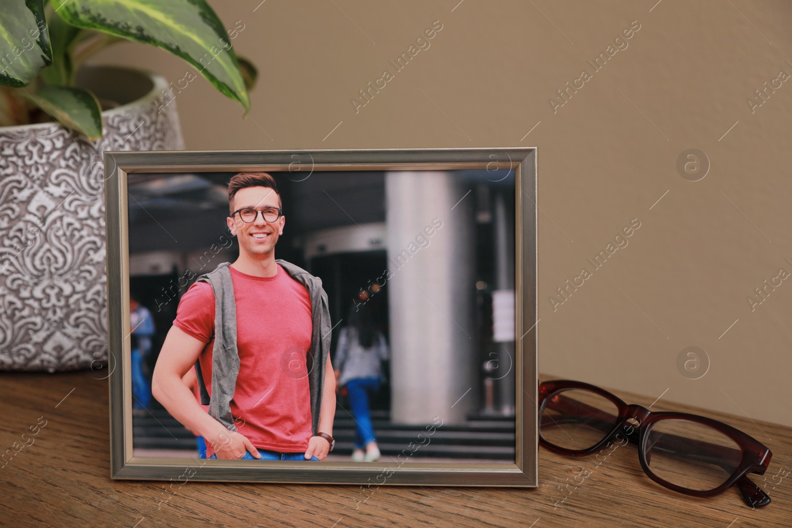 Photo of Framed photo of happy young man near beautiful houseplant and glasses on wooden table