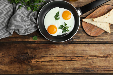 Photo of Tasty cooked chicken eggs with parsley in frying pan on wooden table, flat lay. Space for text