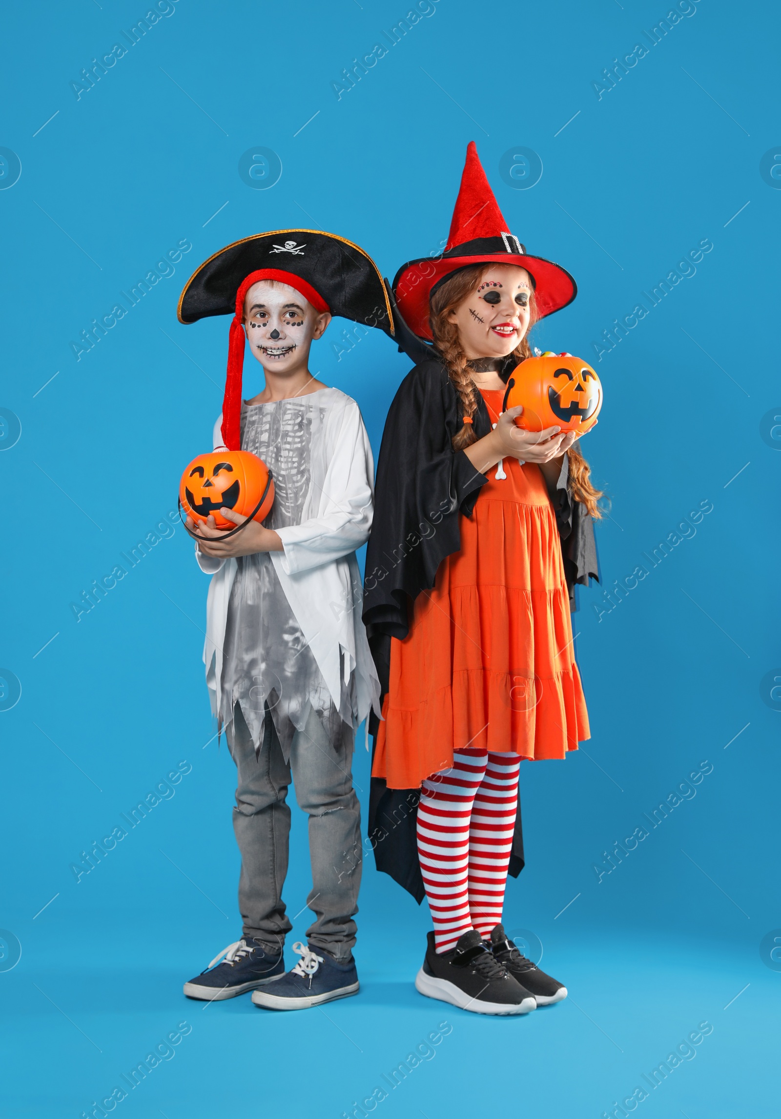 Photo of Cute little kids with pumpkin candy buckets wearing Halloween costumes on blue background