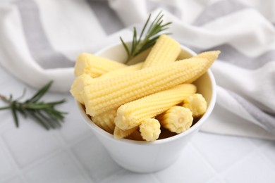 Photo of Tasty fresh yellow baby corns in bowl on white tiled table, closeup