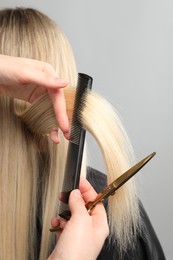Photo of Hairdresser combing and cutting client's hair on light grey background, closeup
