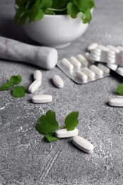 Photo of Pills and mortar with fresh green celandine on light grey table