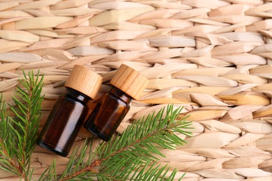 Photo of Bottles of pine essential oil and branches on wicker surface, flat lay. Space for text