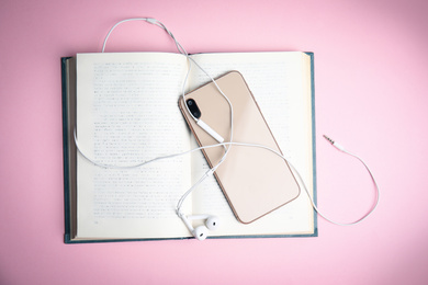 Book, modern headphones and smartphone on pink background, top view