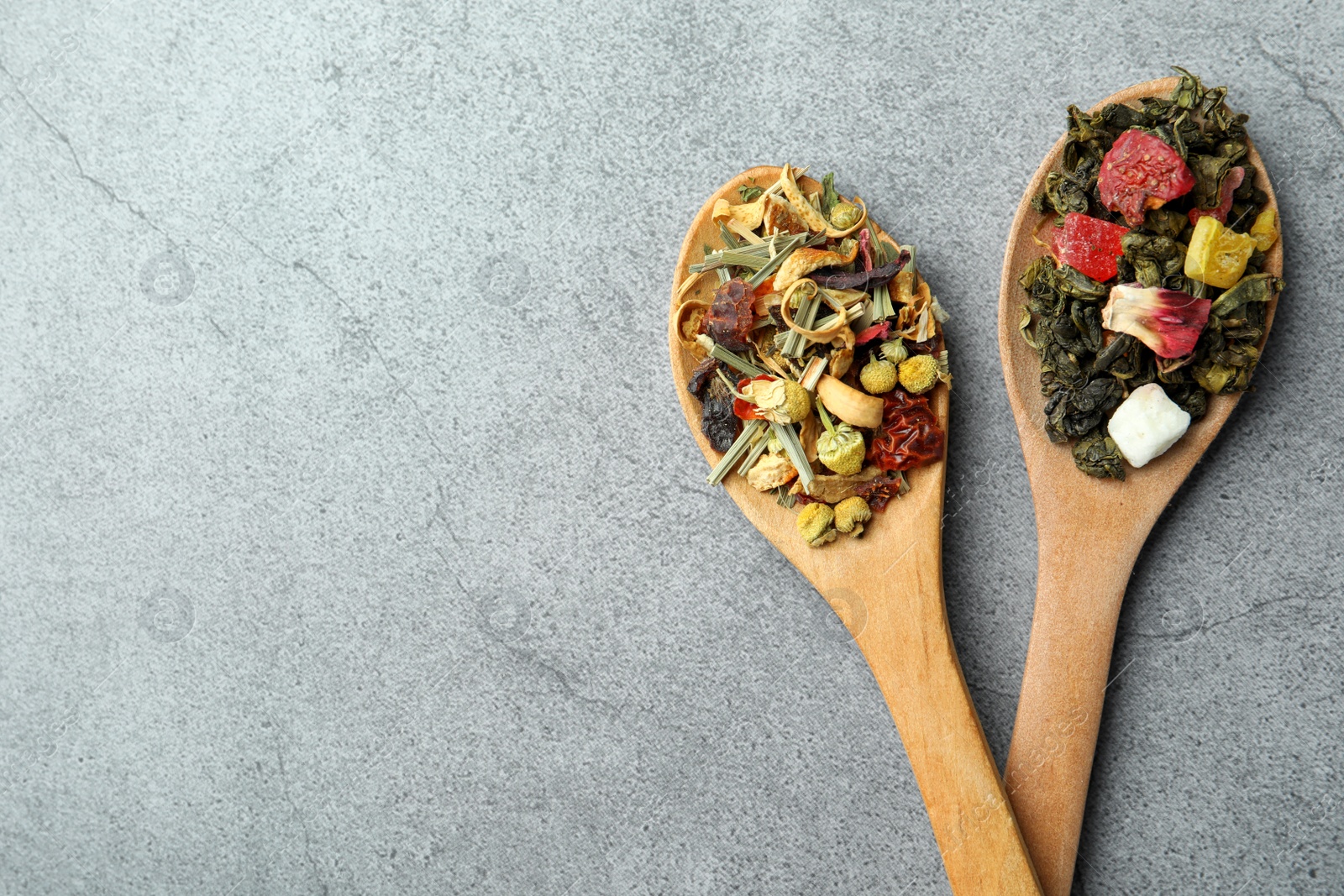 Photo of Different kinds of dry herbal tea in wooden spoons on light grey table, flat lay. Space for text