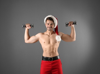 Photo of Shirtless sexy young Santa Claus with dumbbells on color background