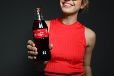 Photo of MYKOLAIV, UKRAINE - NOVEMBER 28, 2018: Young woman with bottle of Coca-Cola on dark background, closeup