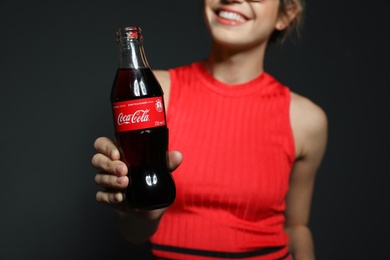 MYKOLAIV, UKRAINE - NOVEMBER 28, 2018: Young woman with bottle of Coca-Cola on dark background, closeup