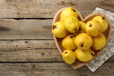 Photo of Tasty ripe quinces in heart shaped bowl on wooden table, top view. Space for text