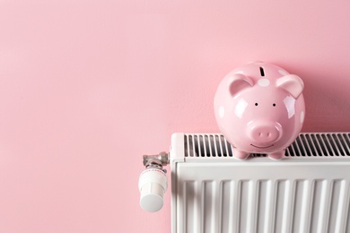 Photo of Heating radiator with piggy bank on color background. Space for text