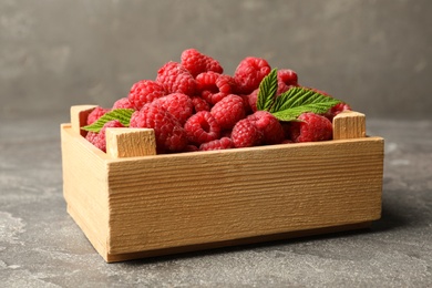 Photo of Wooden crate with delicious ripe raspberries on stone surface