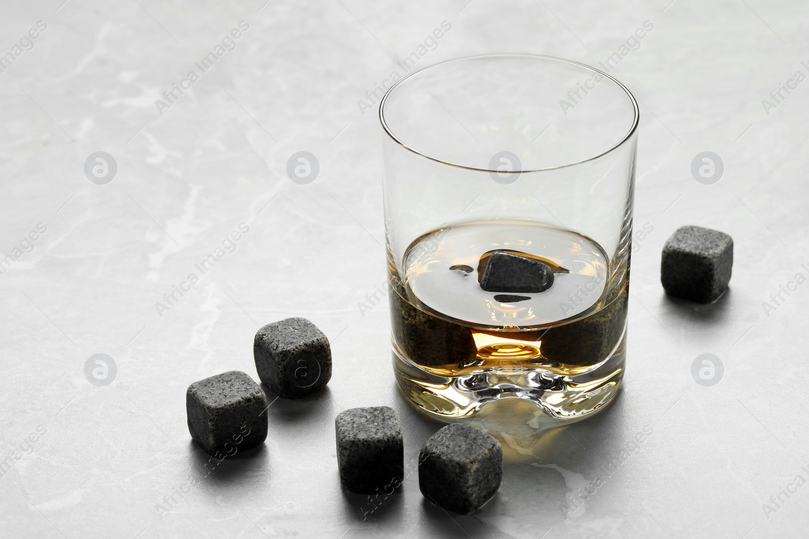 Photo of Whiskey stones and drink in glass on light marble table, closeup. Space for text