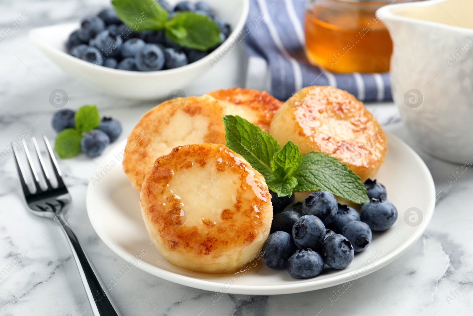 Photo of Delicious cottage cheese pancakes with blueberries, honey and mint on white marble table