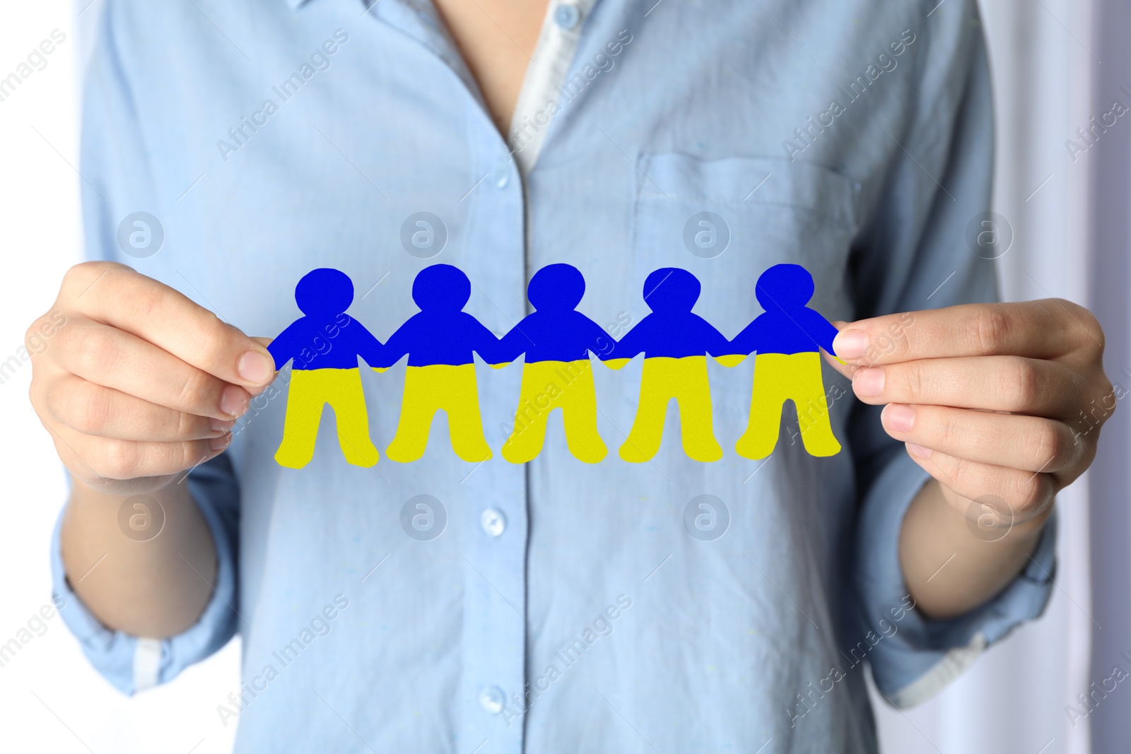 Image of Woman holding paper people chain in colors of Ukrainian flag on light background, closeup