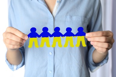 Image of Woman holding paper people chain in colors of Ukrainian flag on light background, closeup