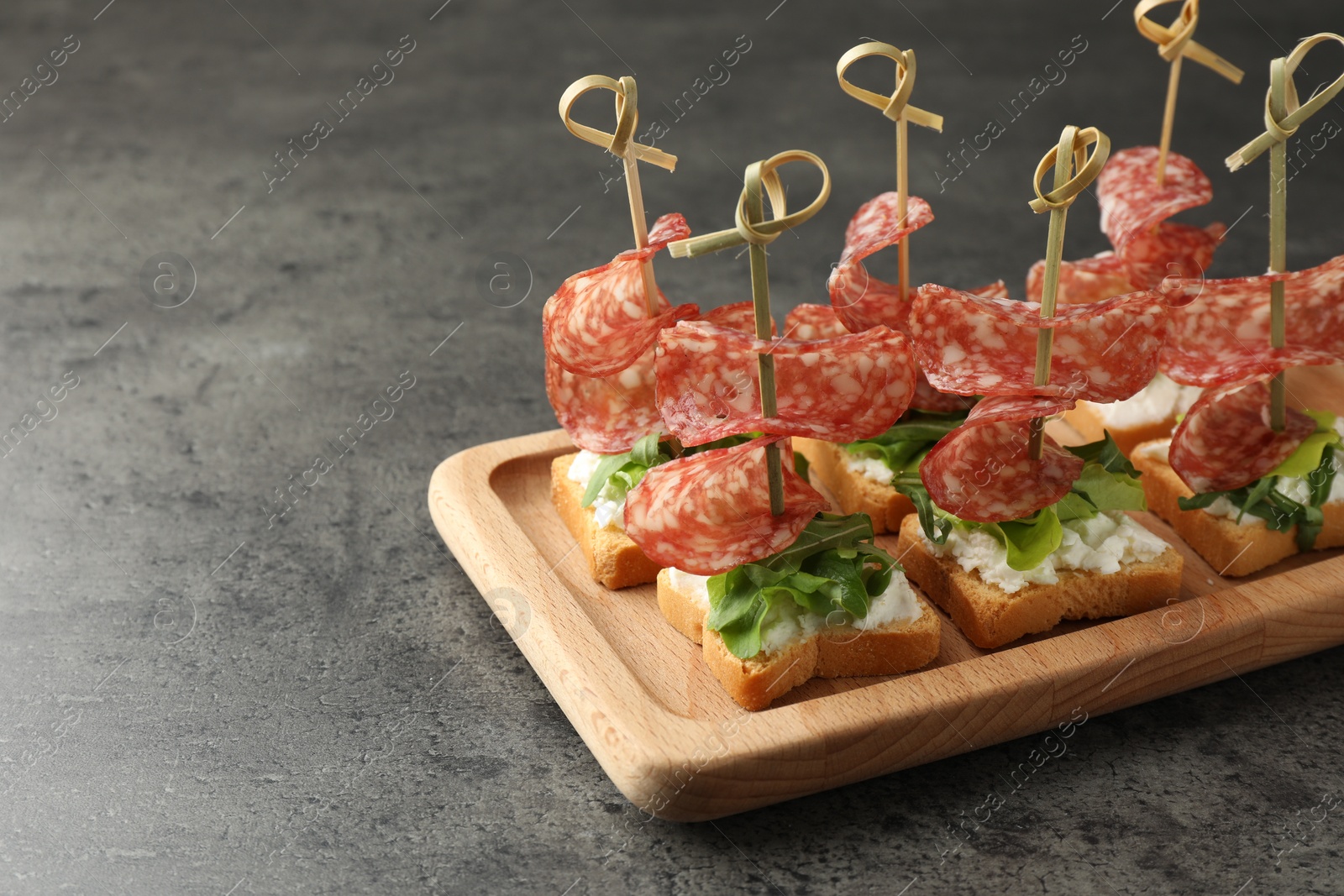 Photo of Tasty canapes with salami, greens and cream cheese on grey table. Space for text