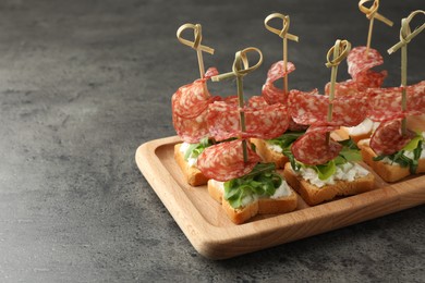 Photo of Tasty canapes with salami, greens and cream cheese on grey table. Space for text