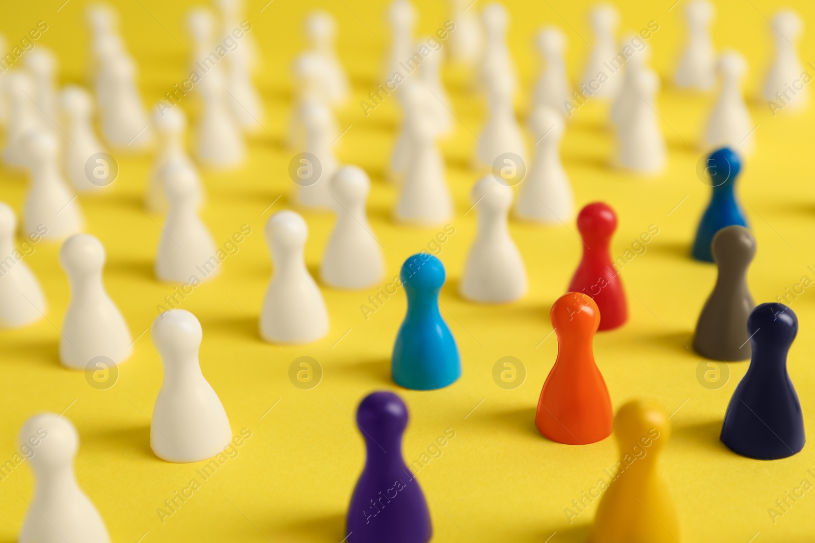 Photo of Colorful pawns on yellow background, closeup. Social inclusion concept