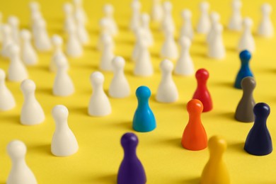 Photo of Colorful pawns on yellow background, closeup. Social inclusion concept