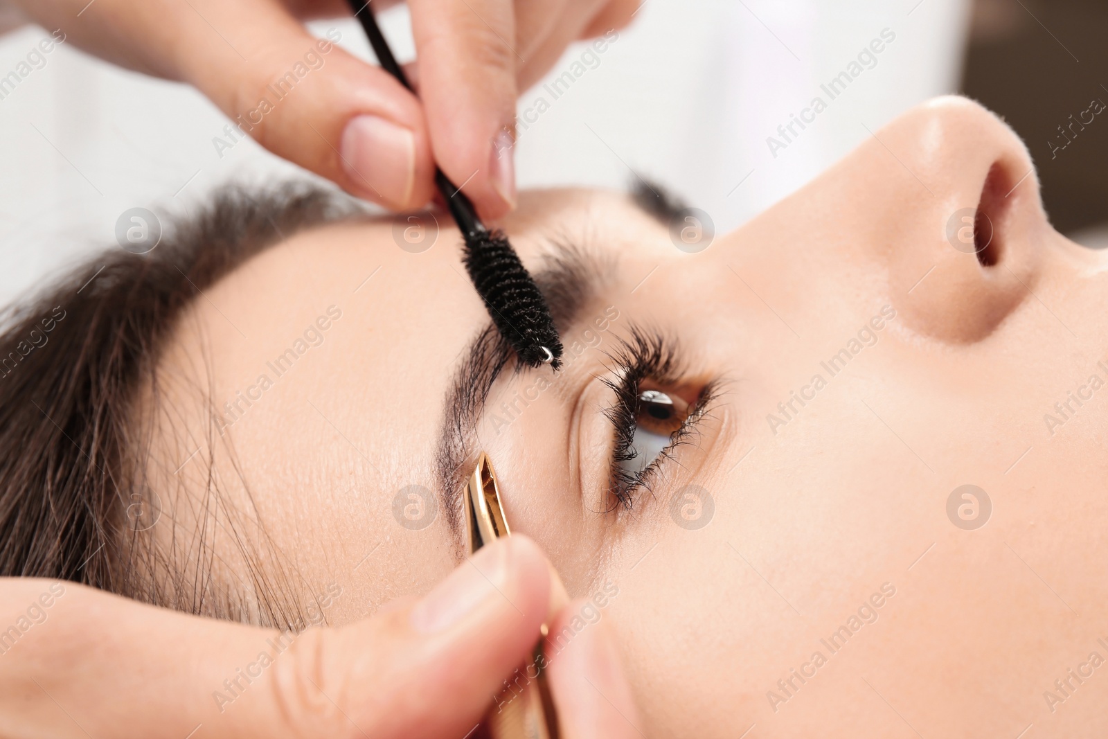 Photo of Young woman having professional eyebrow correction procedure in beauty salon, closeup