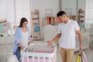 Photo of Happy pregnant woman and her husband with shopping bags choosing crib in store
