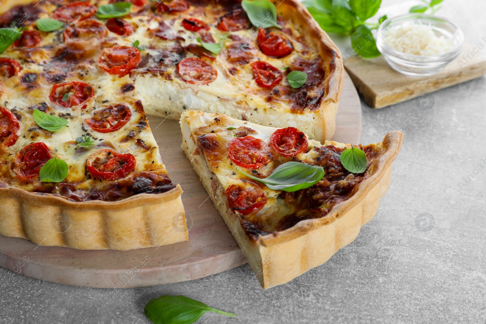 Photo of Cut delicious homemade quiche with prosciutto on light grey table, closeup