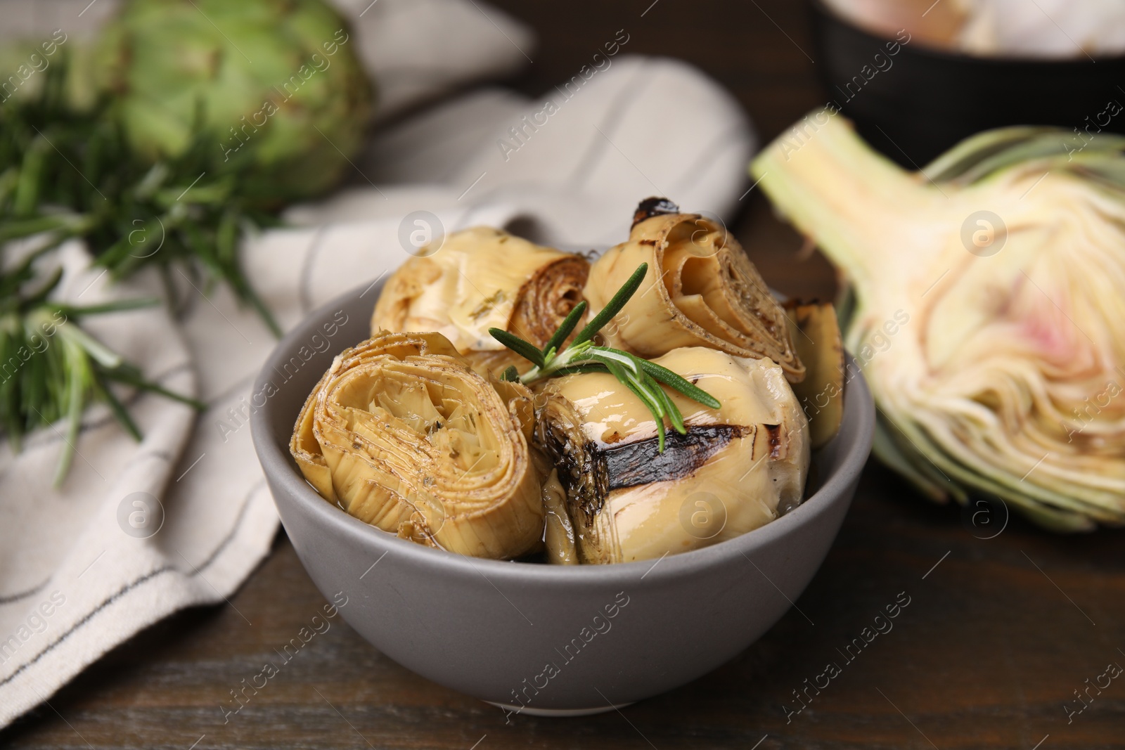 Photo of Bowl with delicious artichokes pickled in olive oil on wooden table, closeup