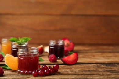 Photo of Jars of different jams and fresh ingredients on wooden table, space for text