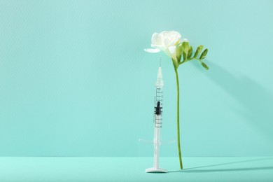Photo of Cosmetology. Medical syringe and freesia flower on turquoise background, space for text