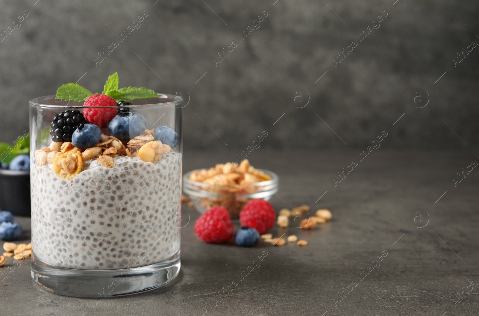 Photo of Delicious chia pudding with berries, granola and mint on grey table, space for text