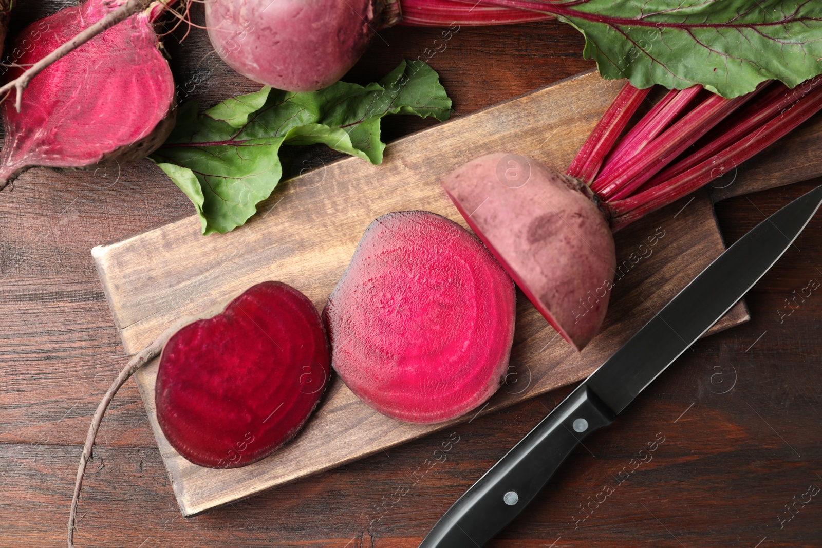 Photo of Cut raw beets and knife on wooden table, flat lay