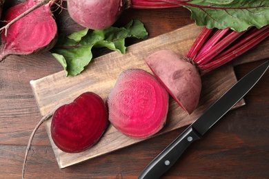 Cut raw beets and knife on wooden table, flat lay