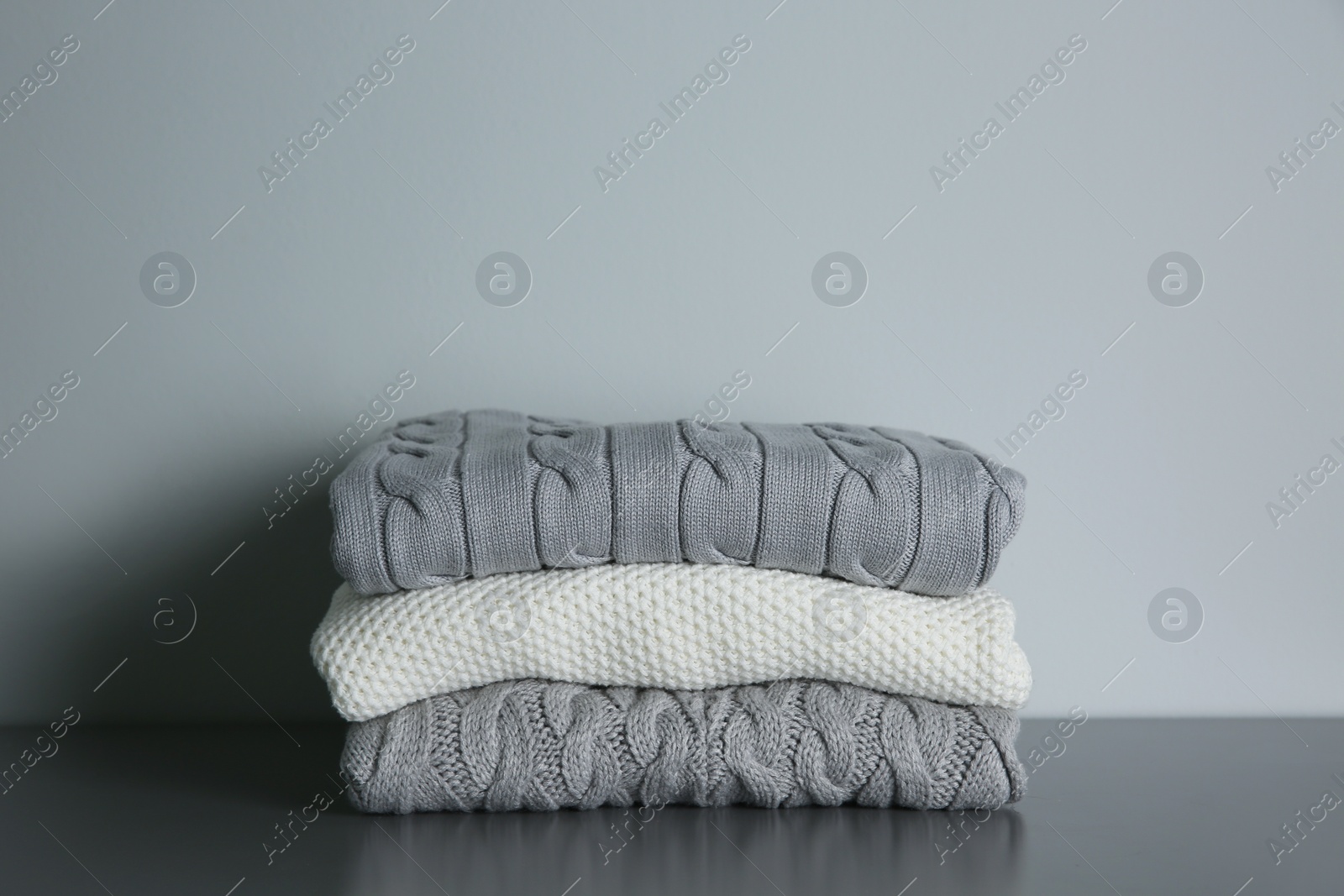 Photo of Stack of folded knitted sweaters on grey table