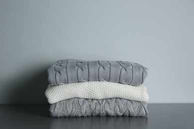 Stack of folded knitted sweaters on grey table