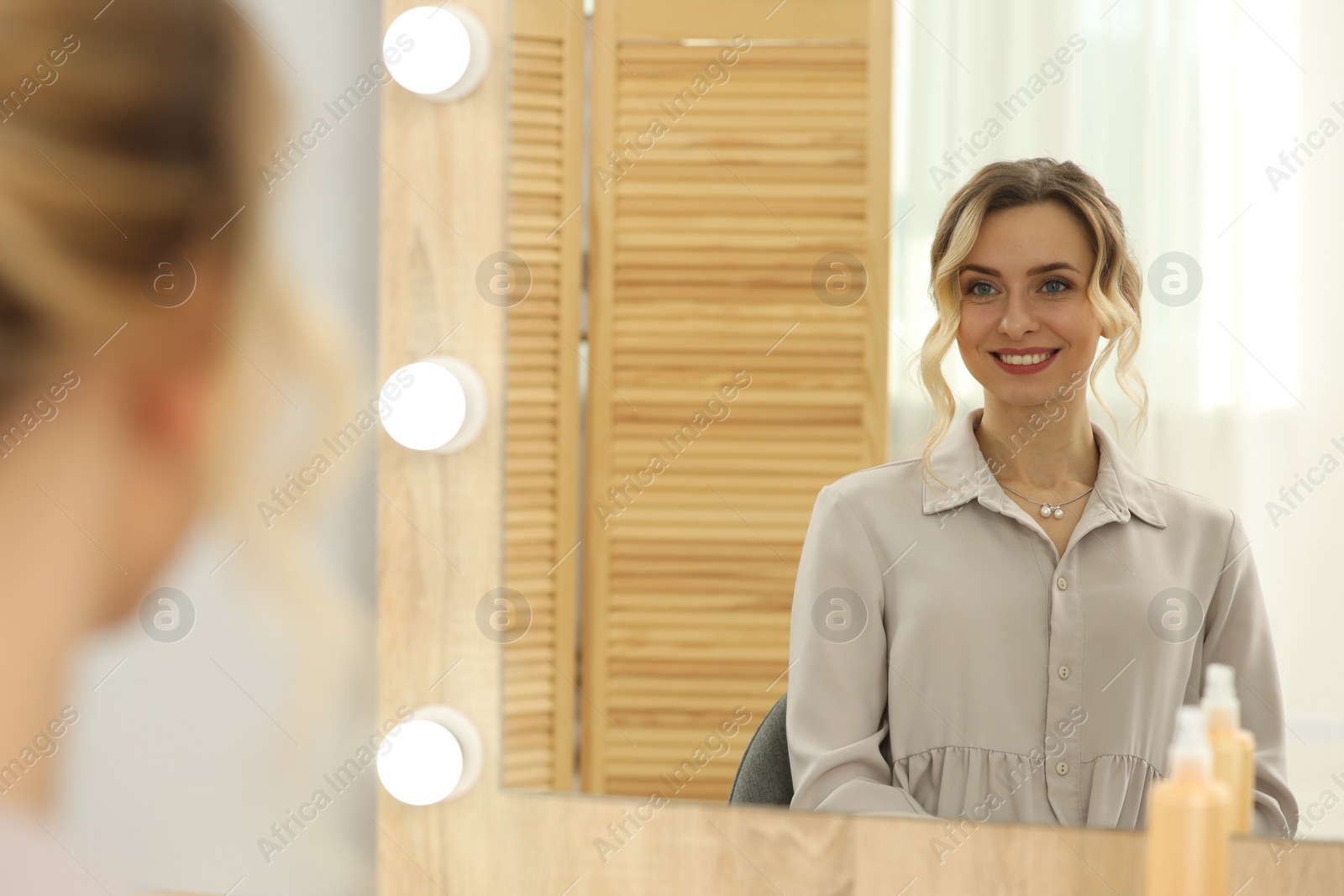 Photo of Smiling woman with beautiful hair style looking at mirror indoors. Space for text