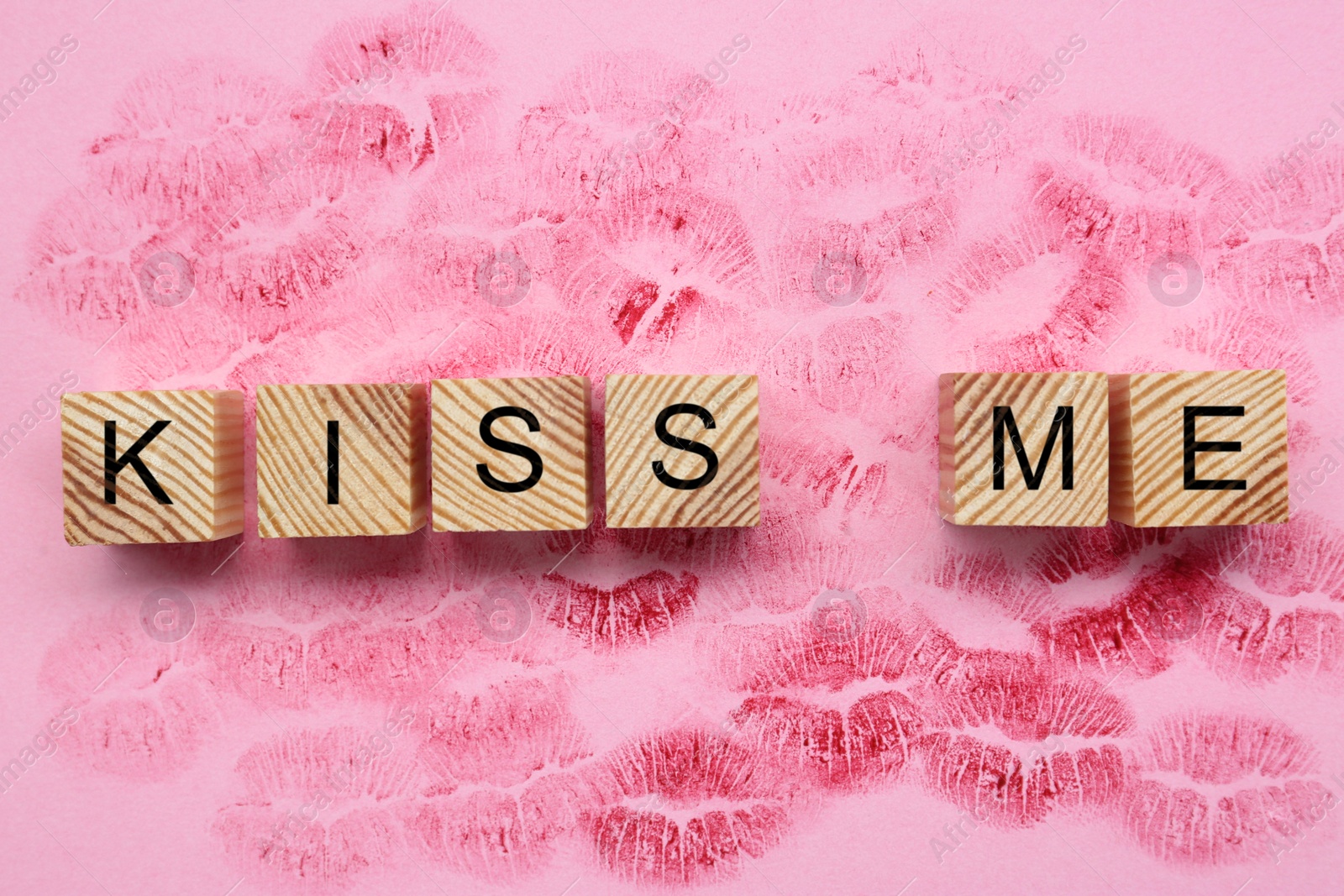 Photo of Wooden cubes with phrase Kiss Me and lipstick marks on pink background, flat lay