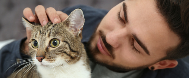 Image of Young man with cat at home, closeup. Banner design