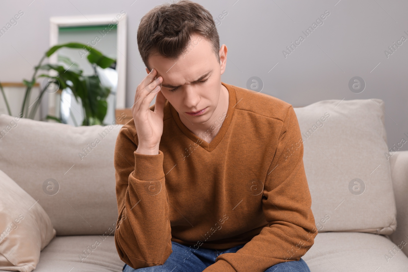 Photo of Sad man suffering from headache on sofa indoors