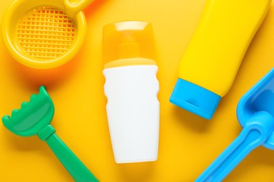 Different suntan products and plastic beach toys on orange background, flat lay