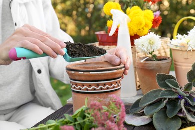Photo of Woman adding fresh soil into pot in garden, closeup