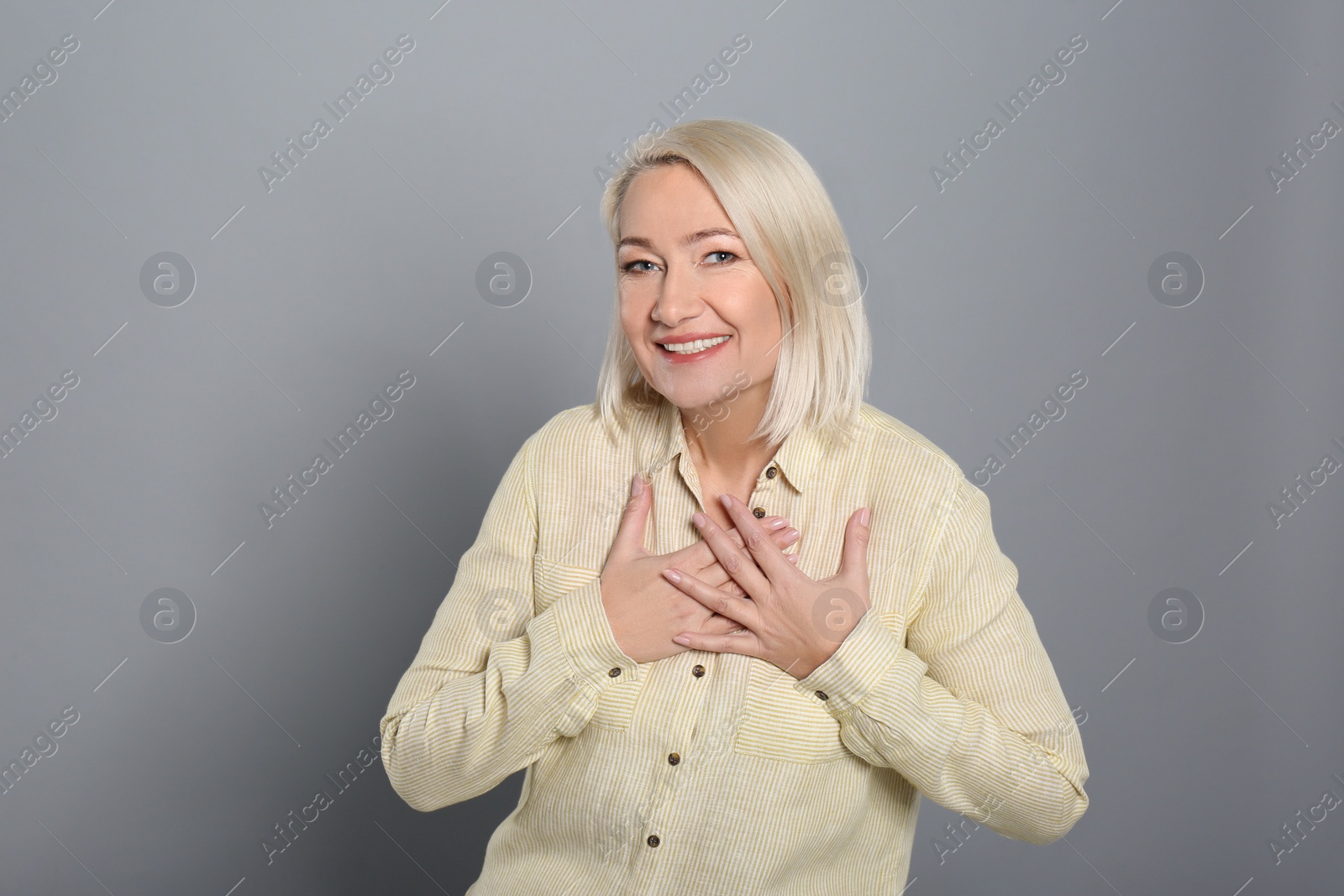 Photo of Happy woman holding hands near heart on grey background